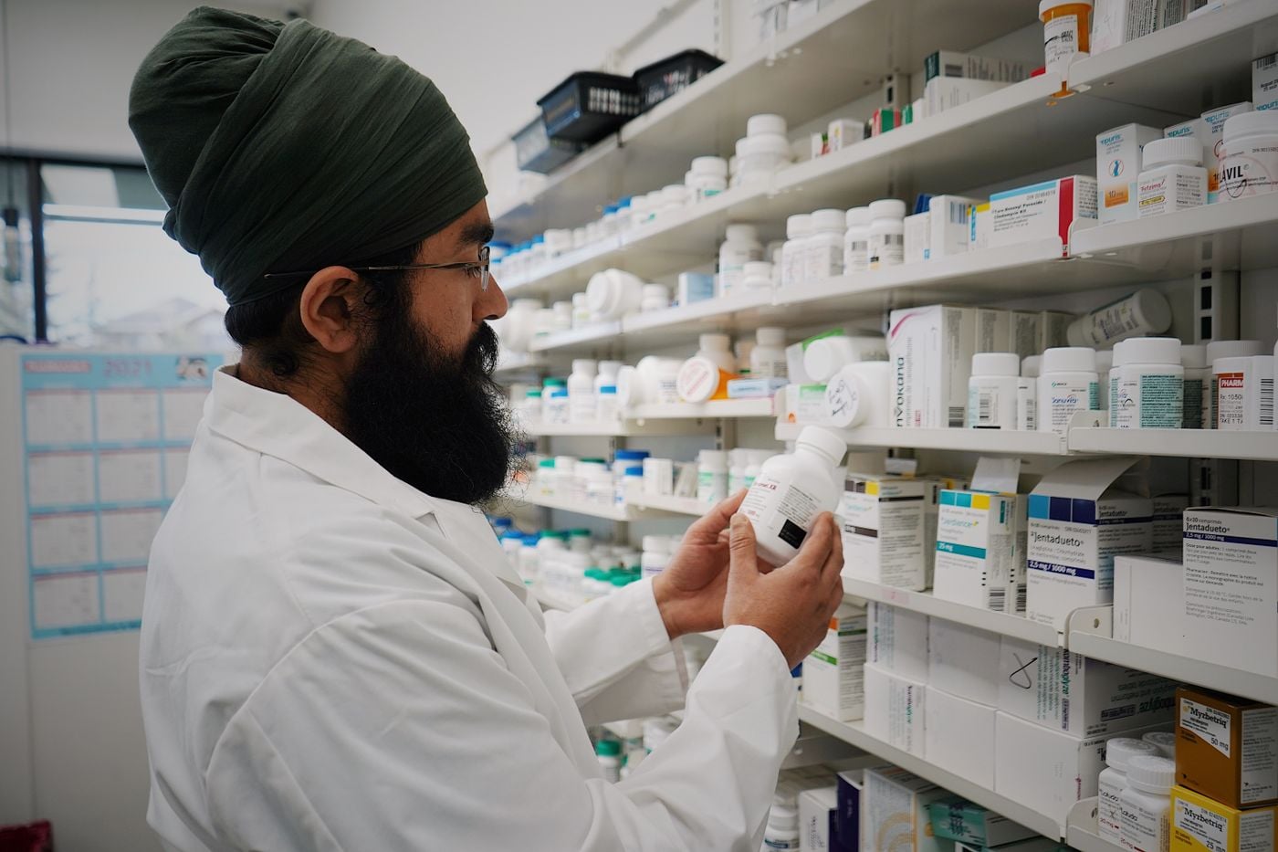 Farmacêutico conferindo uma caixa de remédio diante das prateleiras de uma farmácia